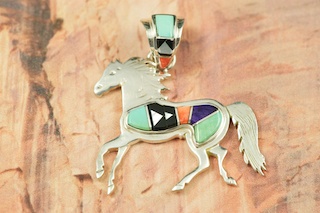 Genuine Turquoise, Spiny Oyster Shell, Sugilite, Blue Lapis and Black Jade inlaid between ribbons of Sterling Silver. Horse Pendant features beautiful inlay work on the bale. Designed by Navajo Artist Calvin Begay. Signed.